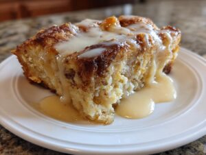 A close-up of a square serving of amazing bread pudding topped with a thick, creamy vanilla sauce.