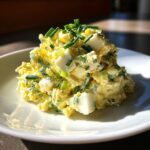 A mound of creamy egg salad recipe topped generously with freshly chopped green chives, served on a white plate.