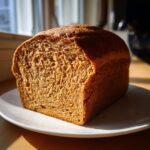 A perfectly baked loaf of whole wheat bread, sliced to show the soft, airy crumb texture, resting on a white plate.