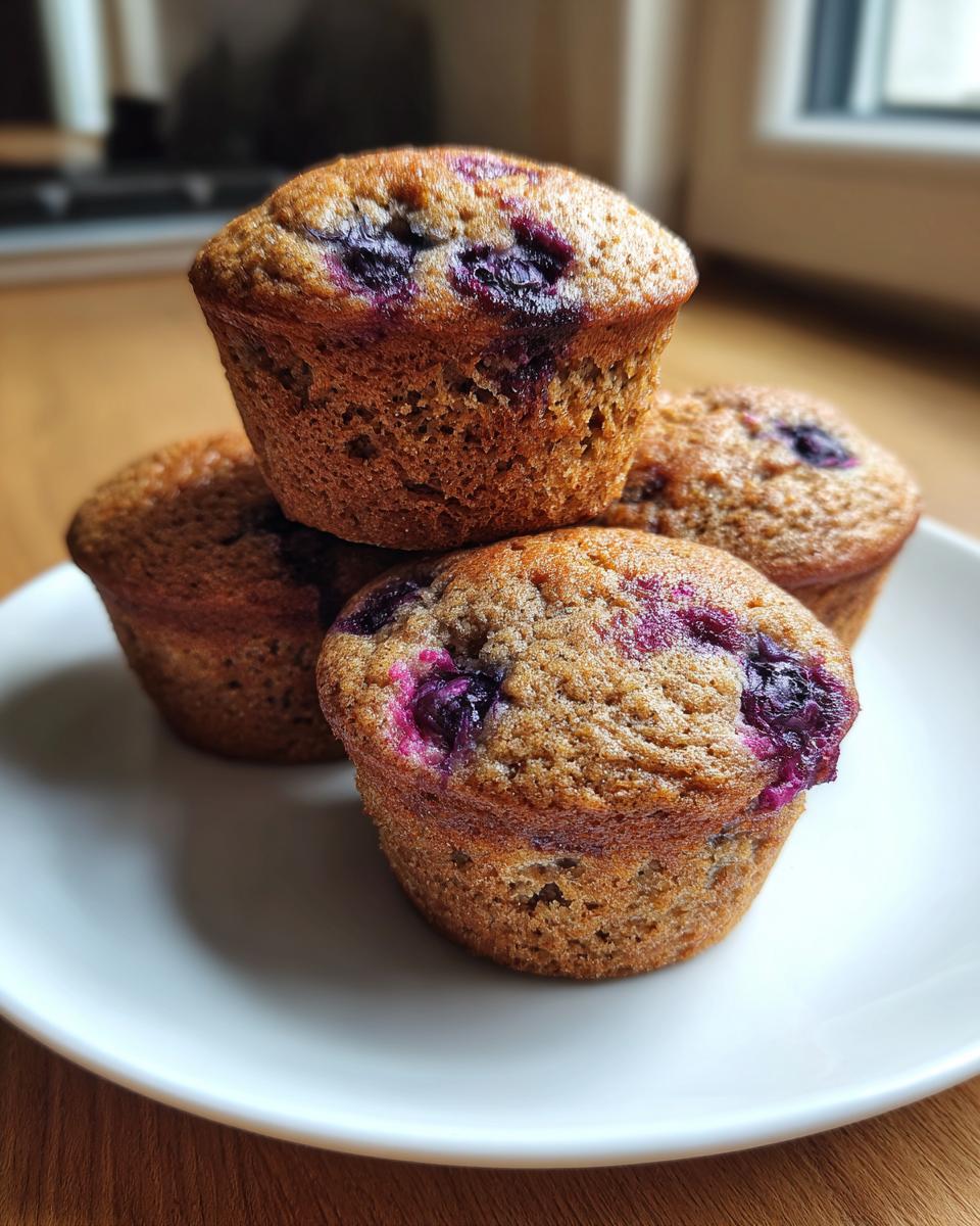A stack of four golden brown blueberry protein muffins resting on a white plate.