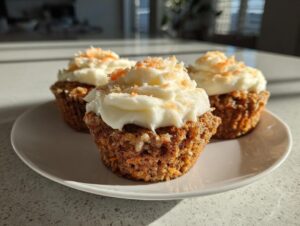 Three delicious carrot cake muffins topped with thick cream cheese frosting and grated carrot sprinkles.
