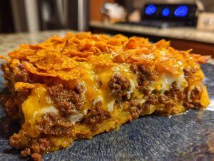A close-up, mouth-watering slice of Dorito Casserole featuring layers of seasoned ground beef, melted cheese, and a crunchy Doritos topping.