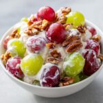 A close-up of creamy chicken salad chick grape salad mixed with red and green grapes and topped with toasted pecans.