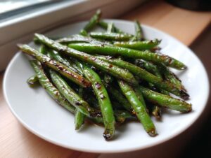 A close-up of blistered chinese green beans with garlic sauce piled on a white plate.