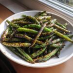 A white bowl filled with blistered chinese green beans with garlic sauce, glistening under natural light.