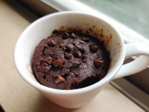 Close-up of a rich, dark chocolate Cottage Cheese Microwave Brownie topped with chocolate chips, served in a white mug.