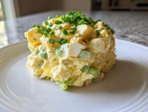 A perfectly molded scoop of creamy egg salad recipe, topped generously with fresh chopped chives.