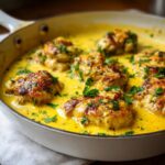 Close-up of seared chicken pieces simmering in a rich, bright yellow creamy lemon chicken sauce, garnished with fresh parsley.