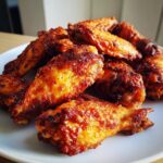 A close-up of a pile of golden brown, crispy baked chicken wings stacked on a white plate.