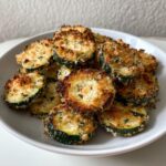 A pile of golden brown, crispy baked parmesan zucchini slices served on a white plate.