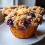 A close-up, appetizing shot of a golden blueberry muffin topped with brown sugar streusel.