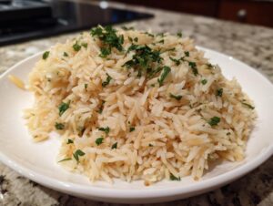 A close-up of fluffy, perfectly cooked rice pilaf served on a white plate and topped with fresh chopped parsley.