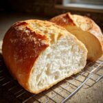 Close-up of freshly baked French bread cut in half, showing the soft white interior crumb cooling on a wire rack.