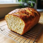 A freshly baked loaf of Italian herb and cheese bread cooling on a wire rack, showing a golden crust and herb flecks inside.
