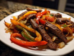 Close-up of perfectly cooked steak fajitas featuring sliced steak, red, yellow, and green bell peppers, and caramelized onions on a white plate.