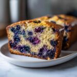 A thick slice of moist blueberry banana bread showing vibrant purple blueberries baked into the golden crumb.