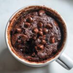Overhead view of a rich, moist chocolate chip mug cake with melted chips inside a white mug.
