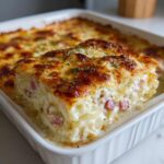 A thick, cheesy slice of scalloped potatoes and ham lifted from a white baking dish, showing layers of potato and ham.