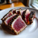 Close-up of perfectly Seared Ahi Tuna slices, crusted with black and white sesame seeds, showing a rare, pink center.