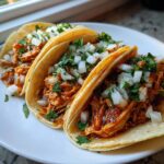 Close-up of three street-style chicken tacos filled with shredded meat and topped generously with diced white onion and cilantro.
