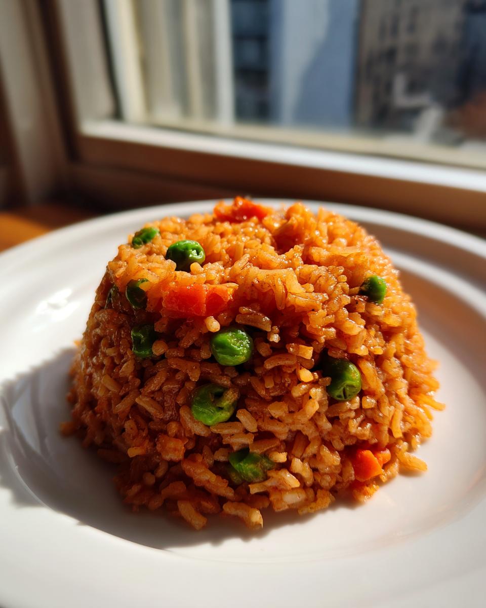 A mound of flavorful, reddish-orange Spanish rice mixed with bright green peas and diced carrots served on a white plate.