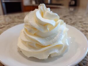 A beautiful, tall swirl of creamy white vanilla buttercream frosting piped onto a small white plate.