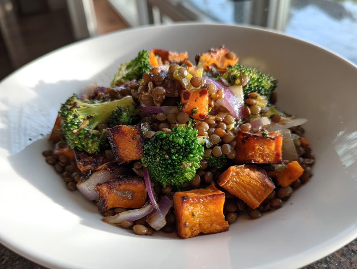 Close-up of a bowl filled with veggie lentil salad featuring brown lentils, roasted sweet potato cubes, broccoli florets, and red onion.