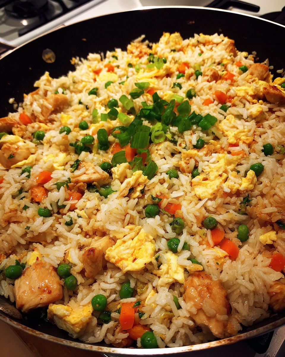 Close-up of homemade chicken fried rice with peas, carrots, scrambled egg, and green onions in a large skillet.