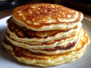 Close-up of a tall stack of five golden brown, fluffy pancakes on a white plate.