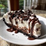 A decadent slice of homemade ice cream pie with chocolate crust, layers, whipped topping, and chocolate drizzle.