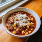A close-up of a white bowl filled with amazing pasta fagioli, featuring ditalini pasta, beans, ground meat, and topped generously with grated Parmesan cheese.