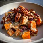 Close-up of cubed sweet potato salad tossed in creamy dressing, topped with pecans, dried cranberries, and seeds.
