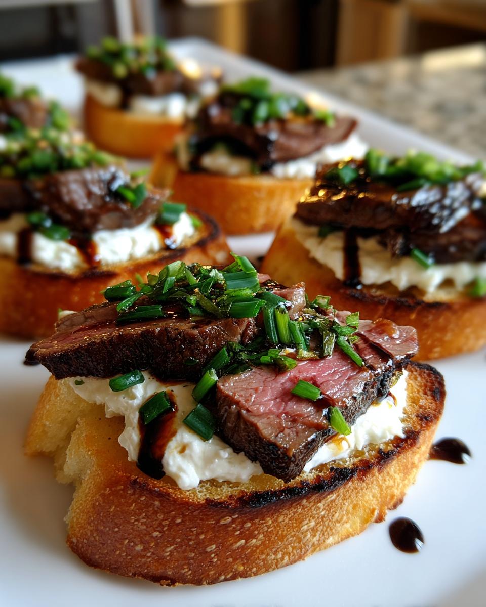 Close-up of a perfectly cooked steak crostini topped with creamy cheese, sliced medium-rare steak, and fresh chives.
