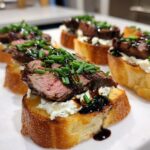 Close-up of perfectly cooked steak crostini topped with creamy cheese, sliced steak, and fresh chives.