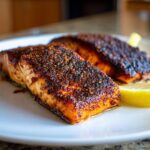 Close-up of two perfectly cooked blackened salmon fillets seasoned with spices, served with a lemon wedge.