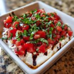 A square white dish filled with creamy cheese topped with diced tomatoes, fresh basil, and a balsamic glaze, showcasing the bruschetta dip.