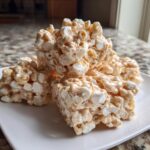 A stack of three square avalanche cookies made with cereal, marshmallows, and a creamy coating, sitting on a white plate.
