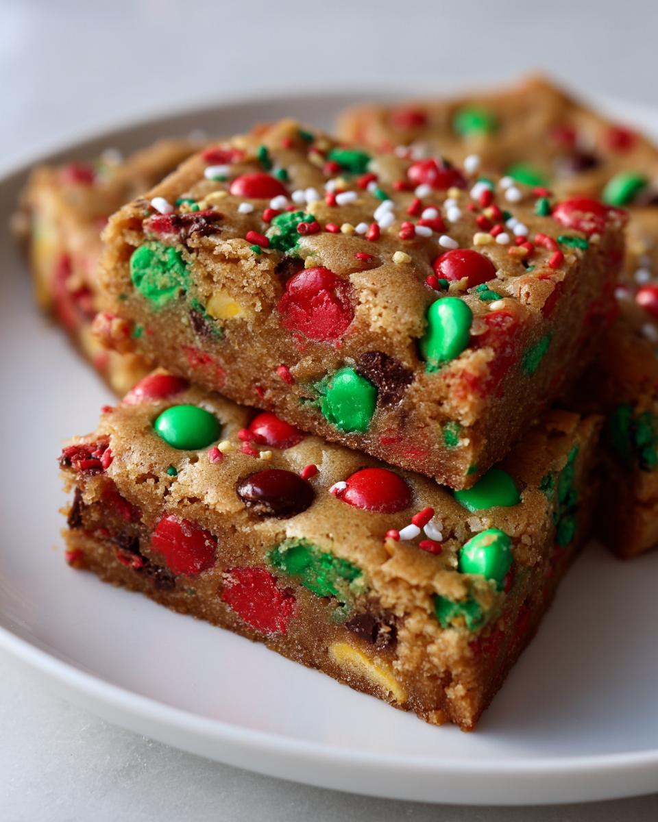 Close-up of stacked, chewy christmas cookie bars loaded with red and green M&Ms and festive sprinkles.