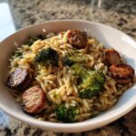 A close-up of a white bowl filled with chicken sausage and broccoli orzo, garnished with parsley.