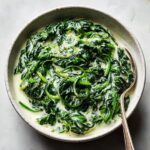 Close-up overhead shot of rich, vibrant green creamed spinach recipe in a rustic bowl with a spoon.