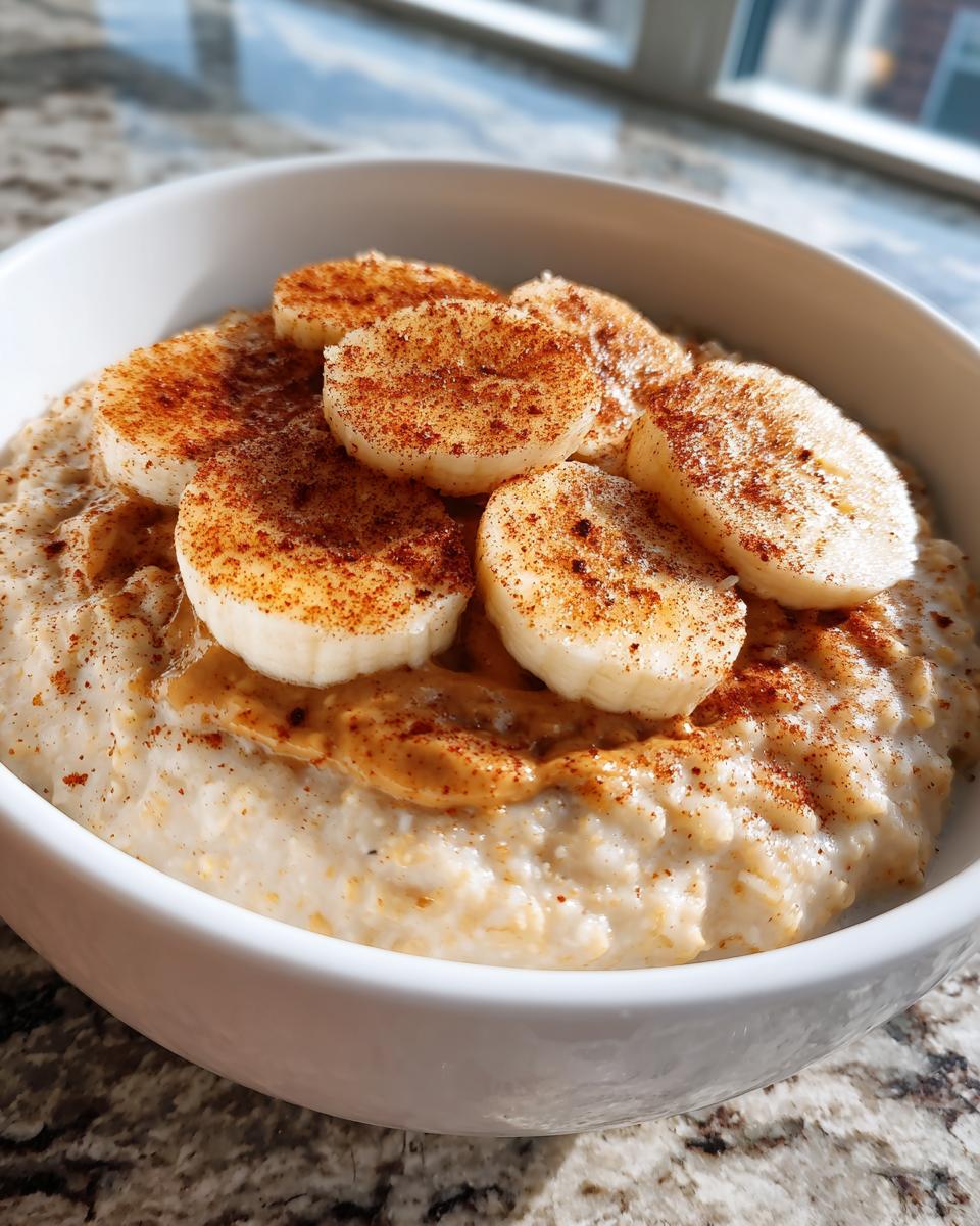 Close-up of creamy banana oatmeal topped with sliced bananas dusted in cinnamon and a swirl of peanut butter.