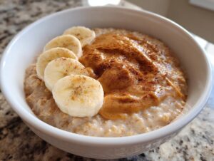 A close-up of creamy banana oatmeal topped with a swirl of peanut butter, sliced bananas, and a sprinkle of cinnamon.