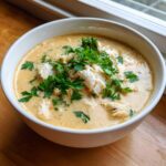 A close-up of a white bowl filled with rich, creamy crab soup, topped generously with flaked crab meat and fresh parsley.