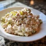 A close-up view of a creamy, chunky ham salad recipe mixed with celery and dressing, served in a white bowl.