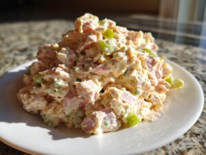 A mound of creamy ham salad recipe featuring diced ham and green celery pieces served on a small white plate.