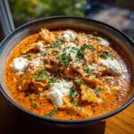 Close-up of a hearty bowl of creamy lasagna soup featuring pasta, rich orange sauce, dollops of ricotta, and fresh parsley.