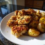 A plate of crispy, breaded garlic parmesan chicken pieces served alongside roasted potatoes.