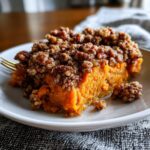 A close-up of a rich, orange slice of crockpot sweet potato casserole topped with a crunchy pecan streusel.