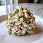 A scoop of creamy dill pickle chicken salad featuring shredded chicken, chopped pickles, red onion, and fresh dill.