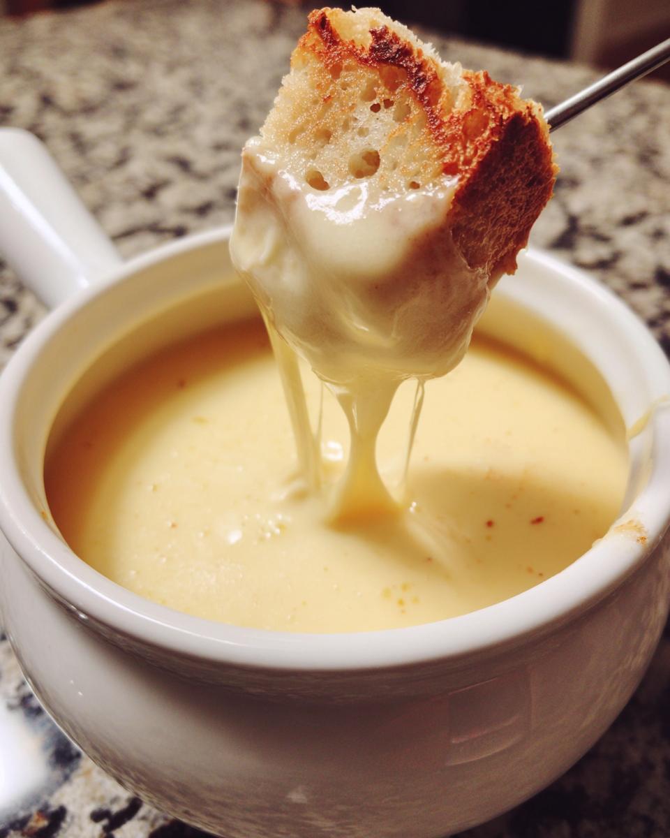 A piece of toasted bread being dipped into a white bowl of smooth, melted cheese fondue.